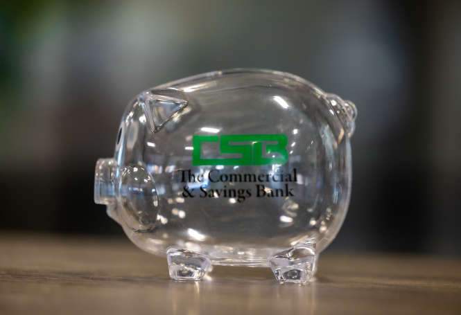 Transparent piggy bank with CSB logo displayed on tabletop.