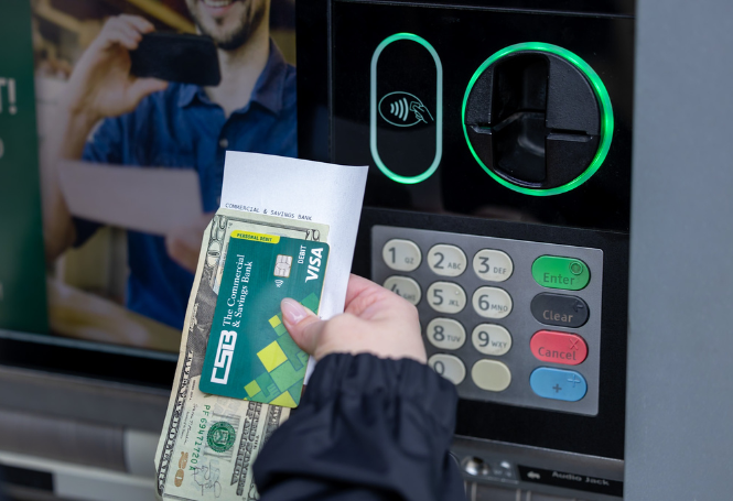 Customer holding CSB debit card, receipt, and cash at drive-thru ATM.