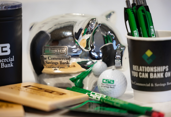 CSB promotional items including piggy bank, pens, golf balls, and branded cup.