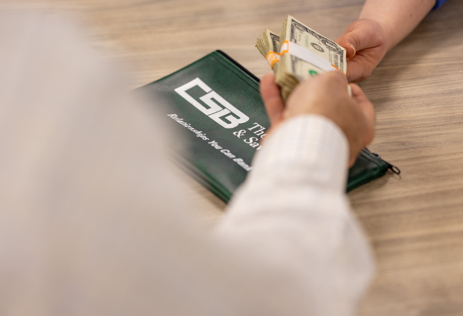 Cash being handed to customer next to CSB branded money pouch