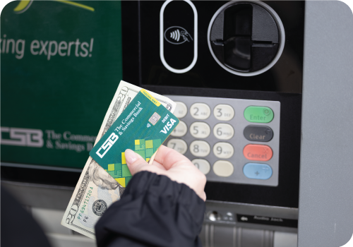 Customer holding cash and a CSB debit card at an ATM.