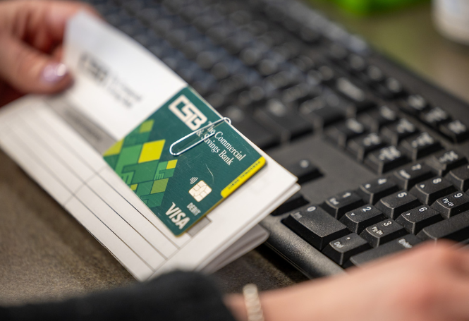Employee holding CSB debit card with account opening information at keyboard.