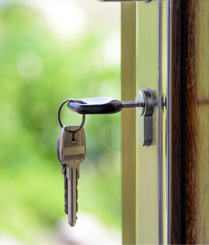 House keys hanging from a door lock with a blurred green background.
