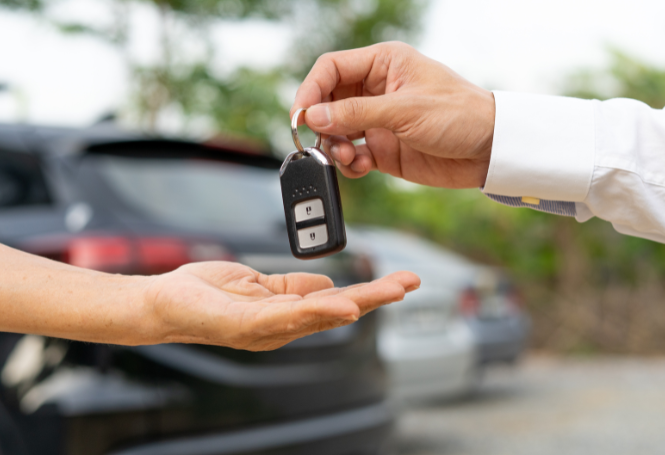 Person handing over a car key fob in a parking lot.