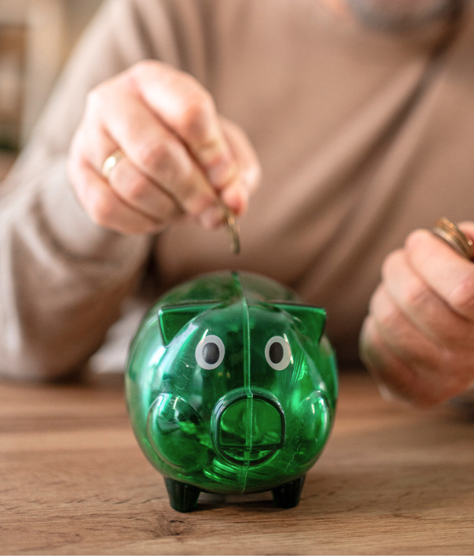 Person placing coins into a green piggy bank to save money.
