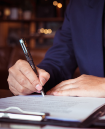 Person signing a document with a pen on a clipboard.