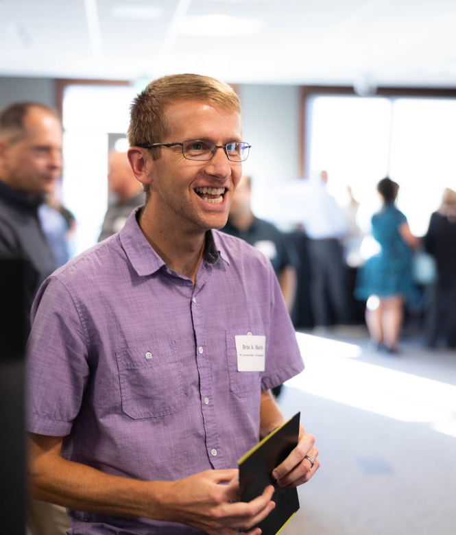 Man smiling at networking event, holding a pamphlet.