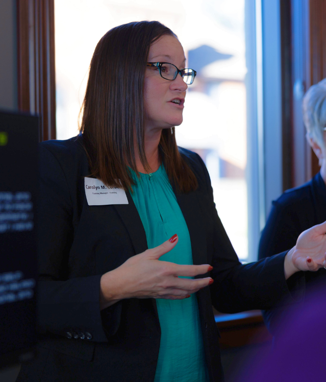 Woman speaking to a group at a professional event near a window.