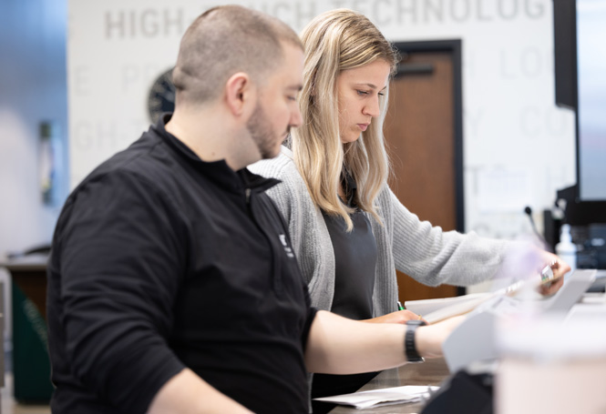 Bank employees reviewing documents behind the teller counter.