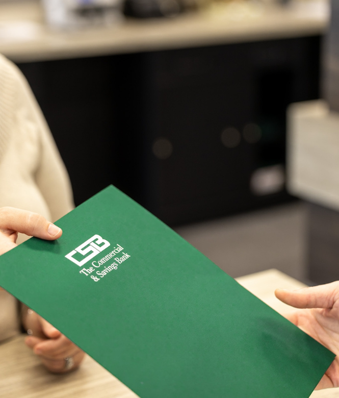 Customer receiving green CSB folder from bank employee