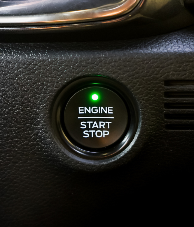 Close-up of a car’s illuminated engine start/stop button with a green indicator light.