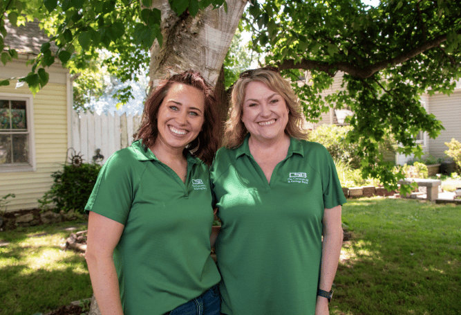 Two Commercial & Savings Bank employees stand outdoors beneath a tree and smile for the camera.